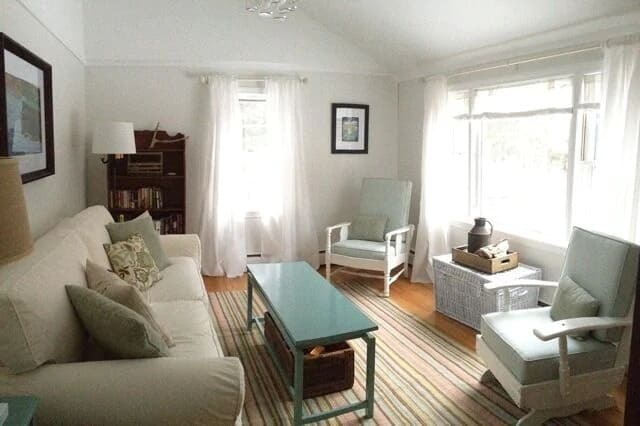 A living room couch, coffee table, and windows with white curtains