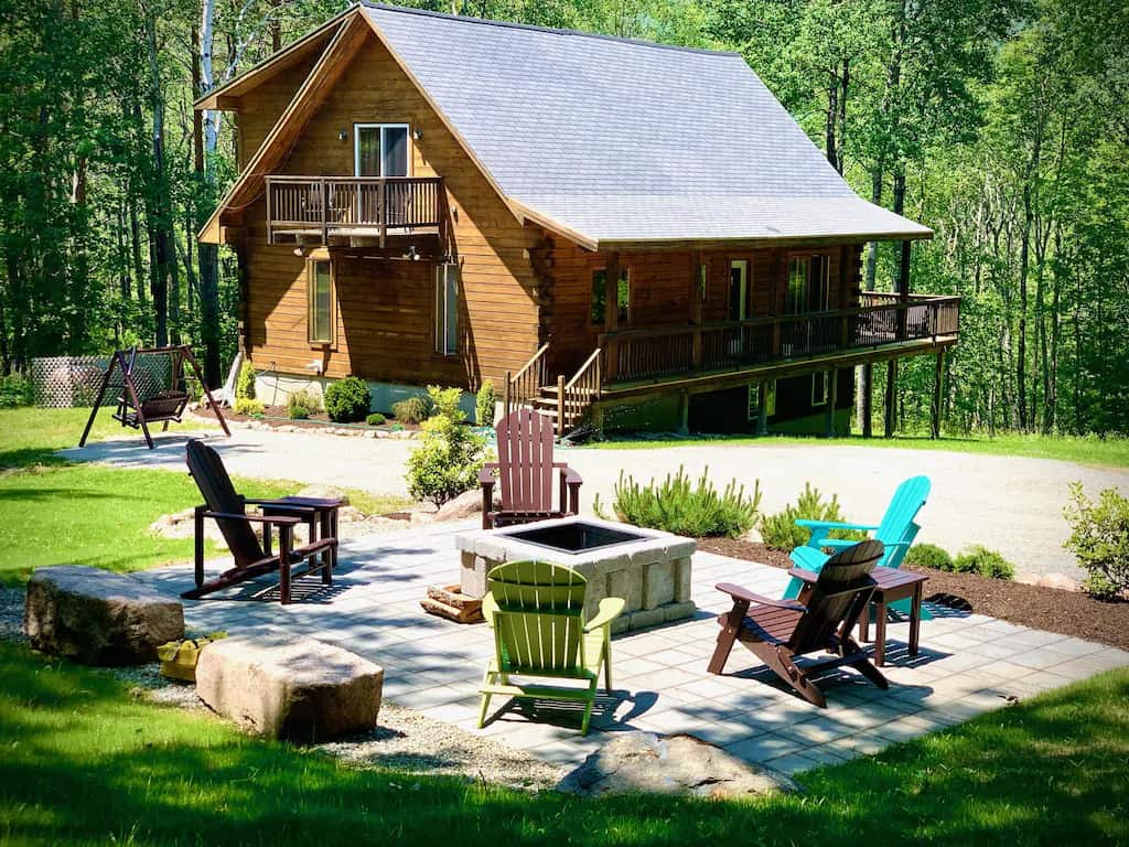 Lawn chairs and a fire pit in front of a large mountain cabin