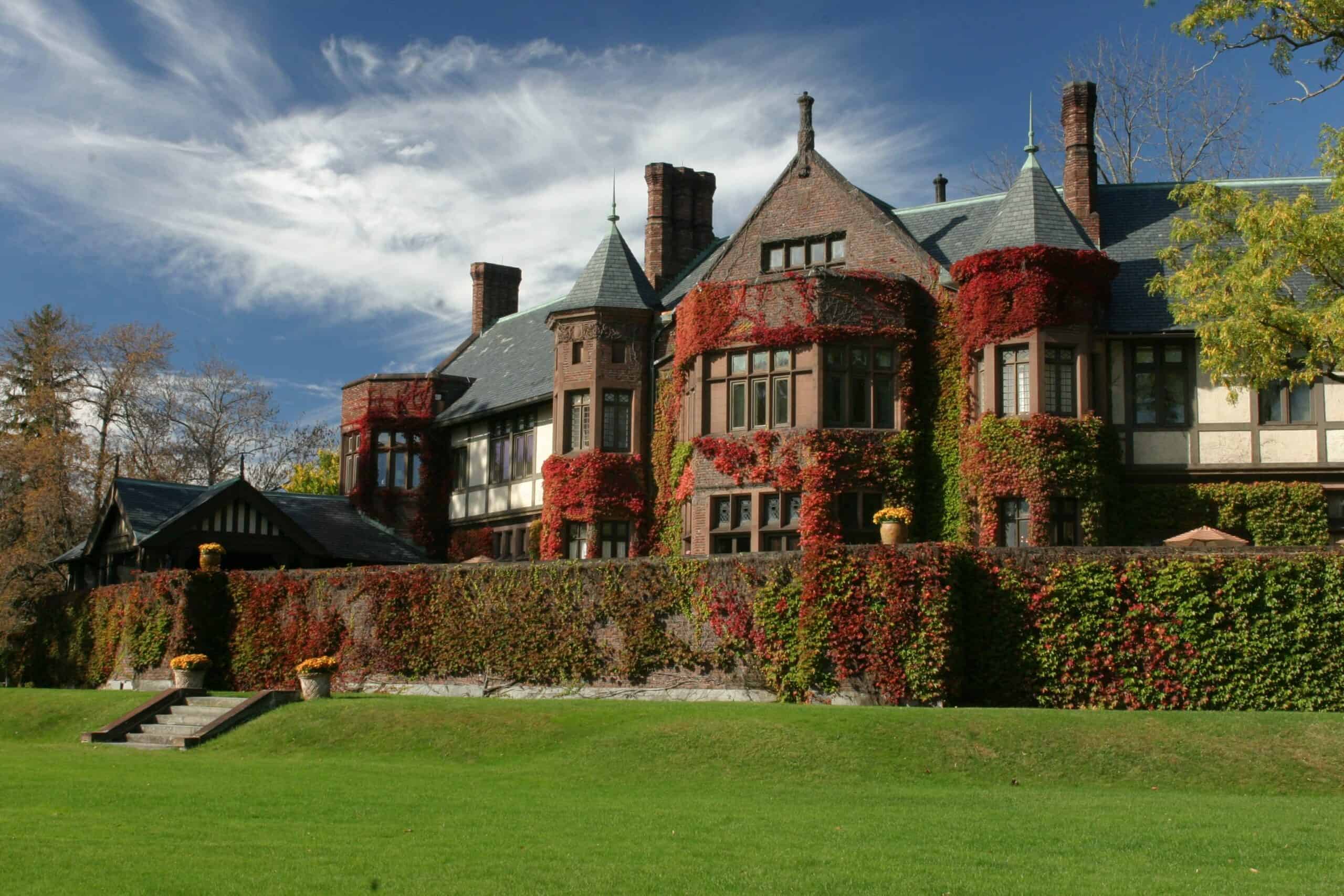 A Tudor style mansion with moss on a fence and a lawn in the foreground