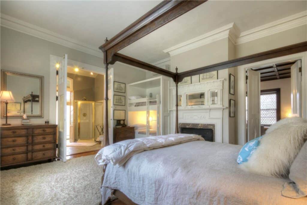 A modern canopy bed in a white bedroom with a fireplace.