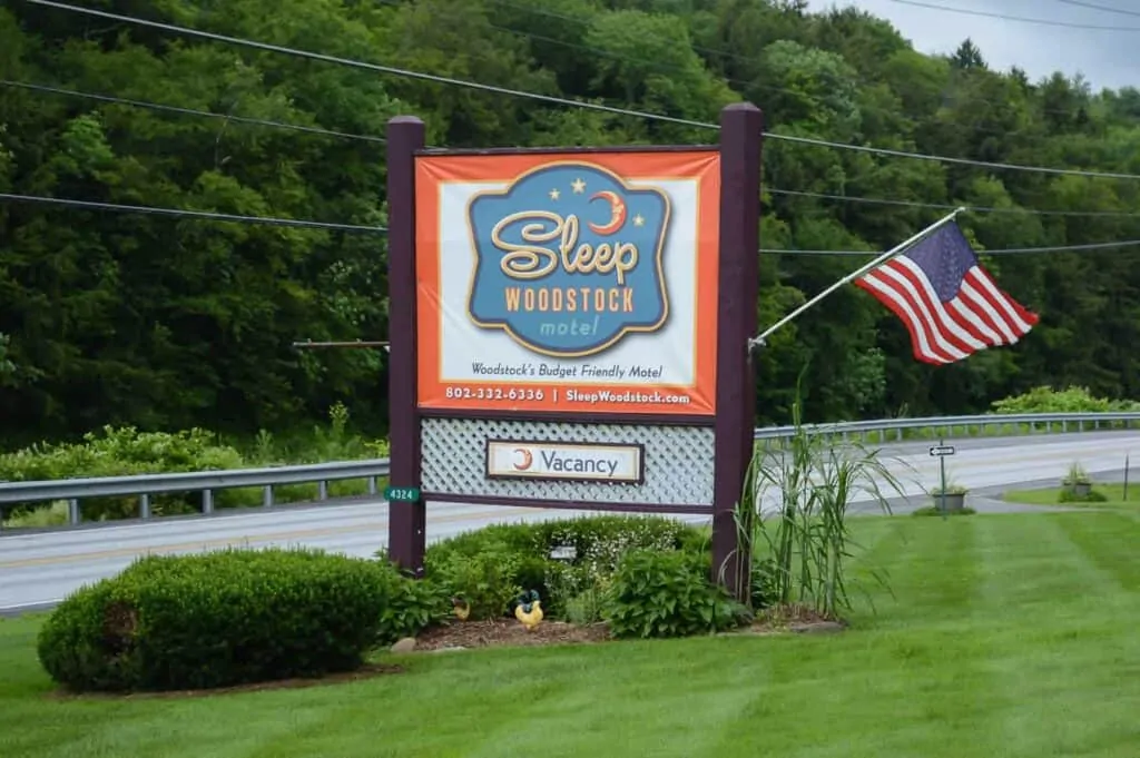A vintage looking sign for a Woodstock motel on a green grassy lawn with an American flag