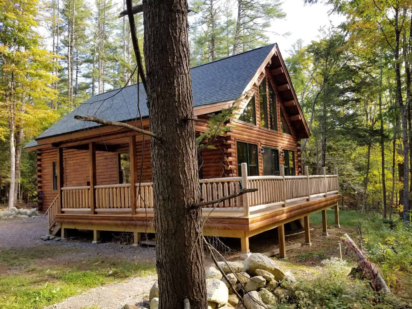 A wooden Massachusetts mountain chalet with a wrap around porch in a woodsy setting.