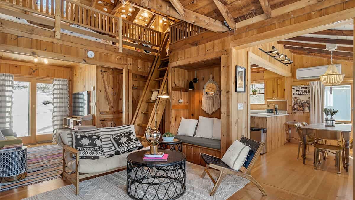An interior with exposed beams and steps leading up to a loft at a Massachusetts cabin