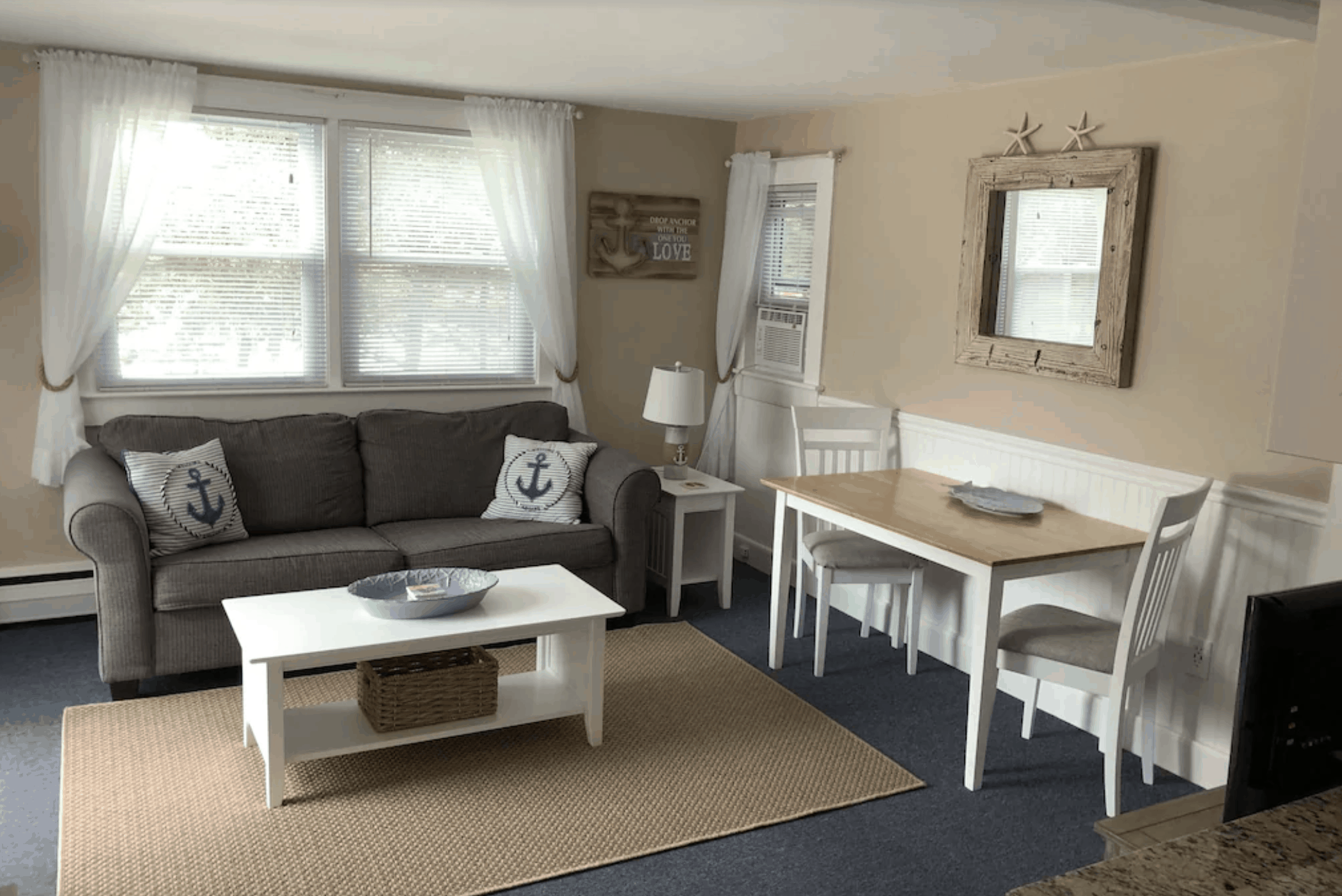 A room in a Massachusetts cabin with a sofa, white coffee table, end table and lamp, and a white table with 2 chairs.