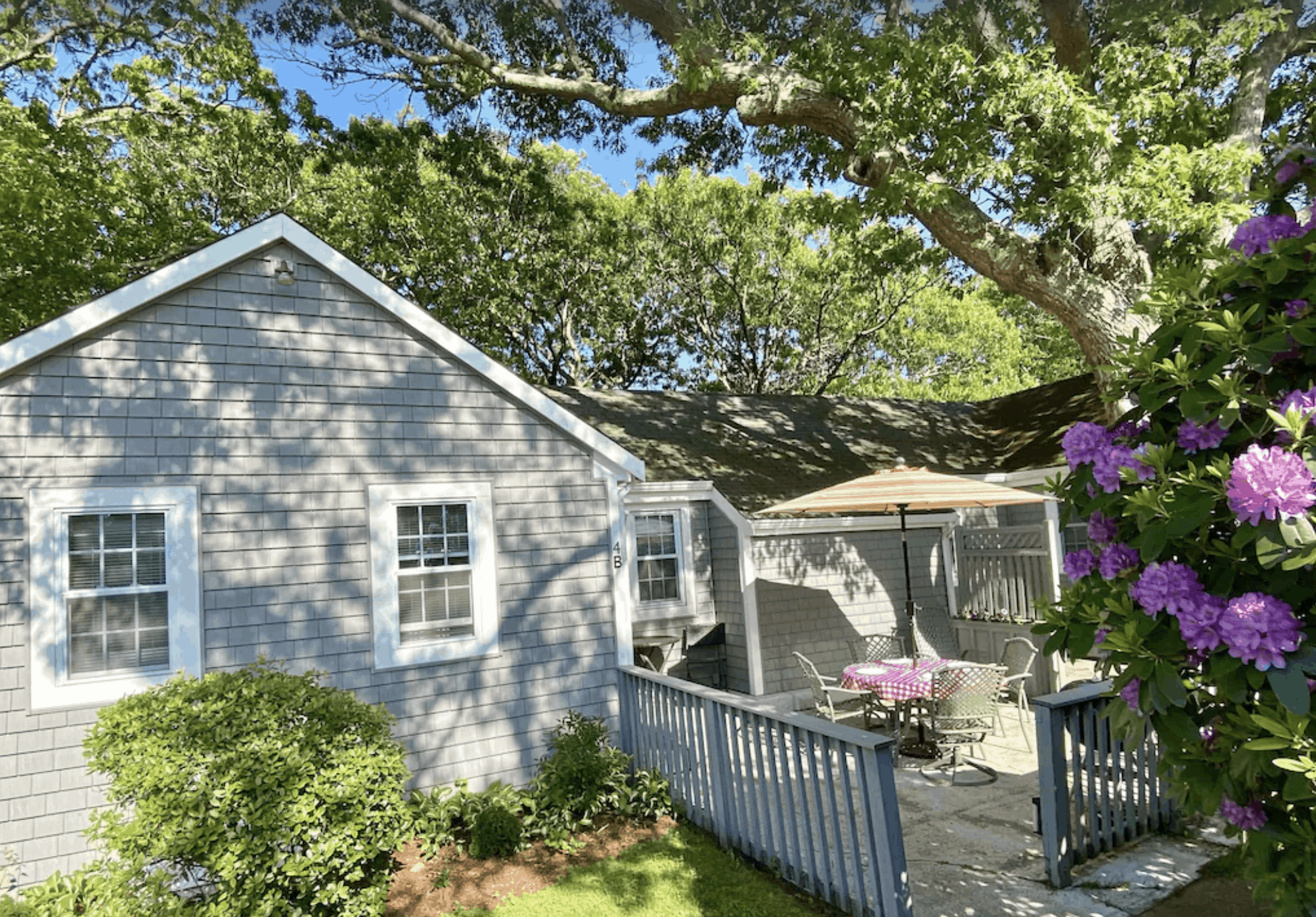 Grey Massachusetts vacation house with a deck and a table with an umbrella; trees all around.