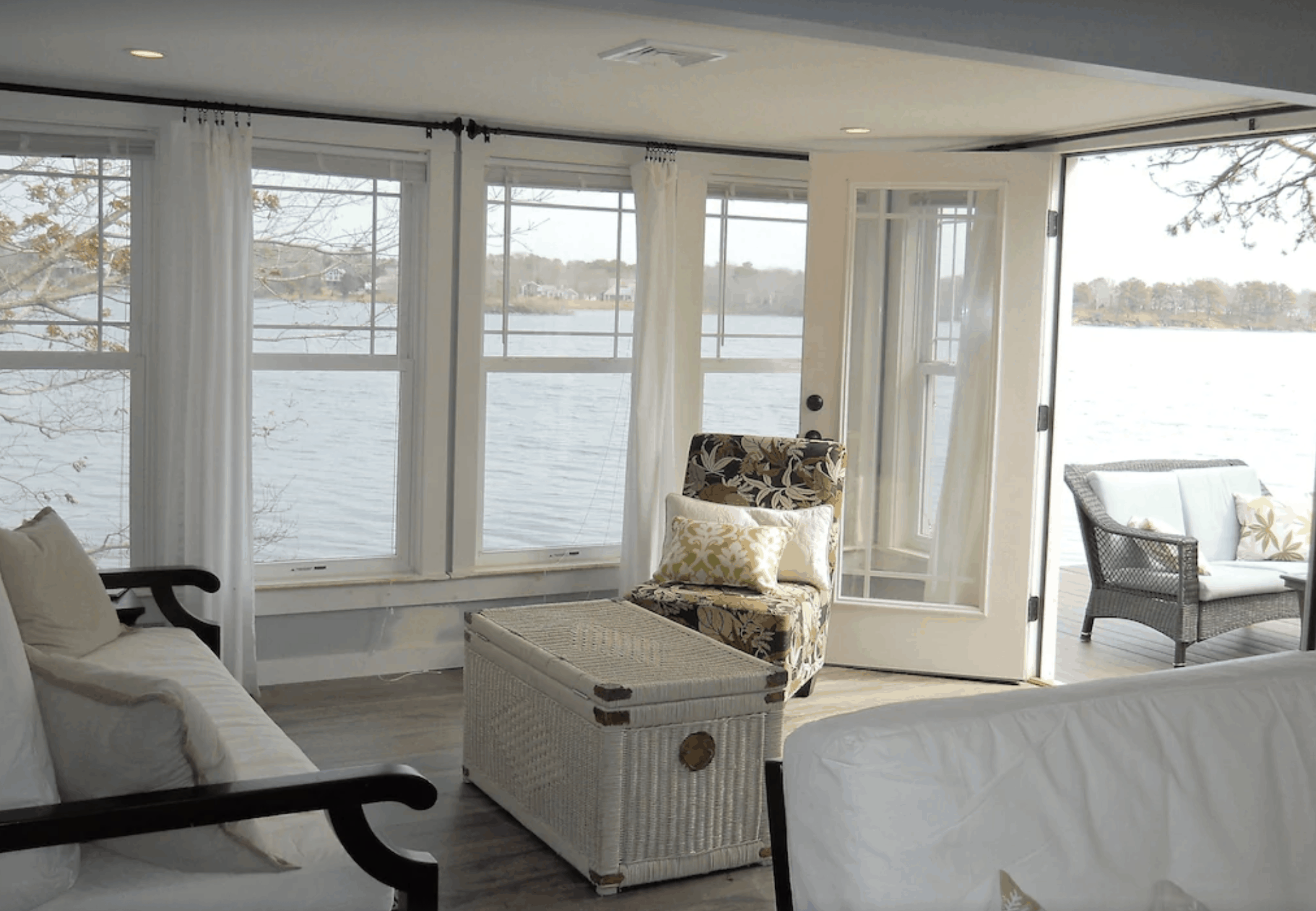 White living room furniture in a coastal MA cabin with lots of windows and an open door.