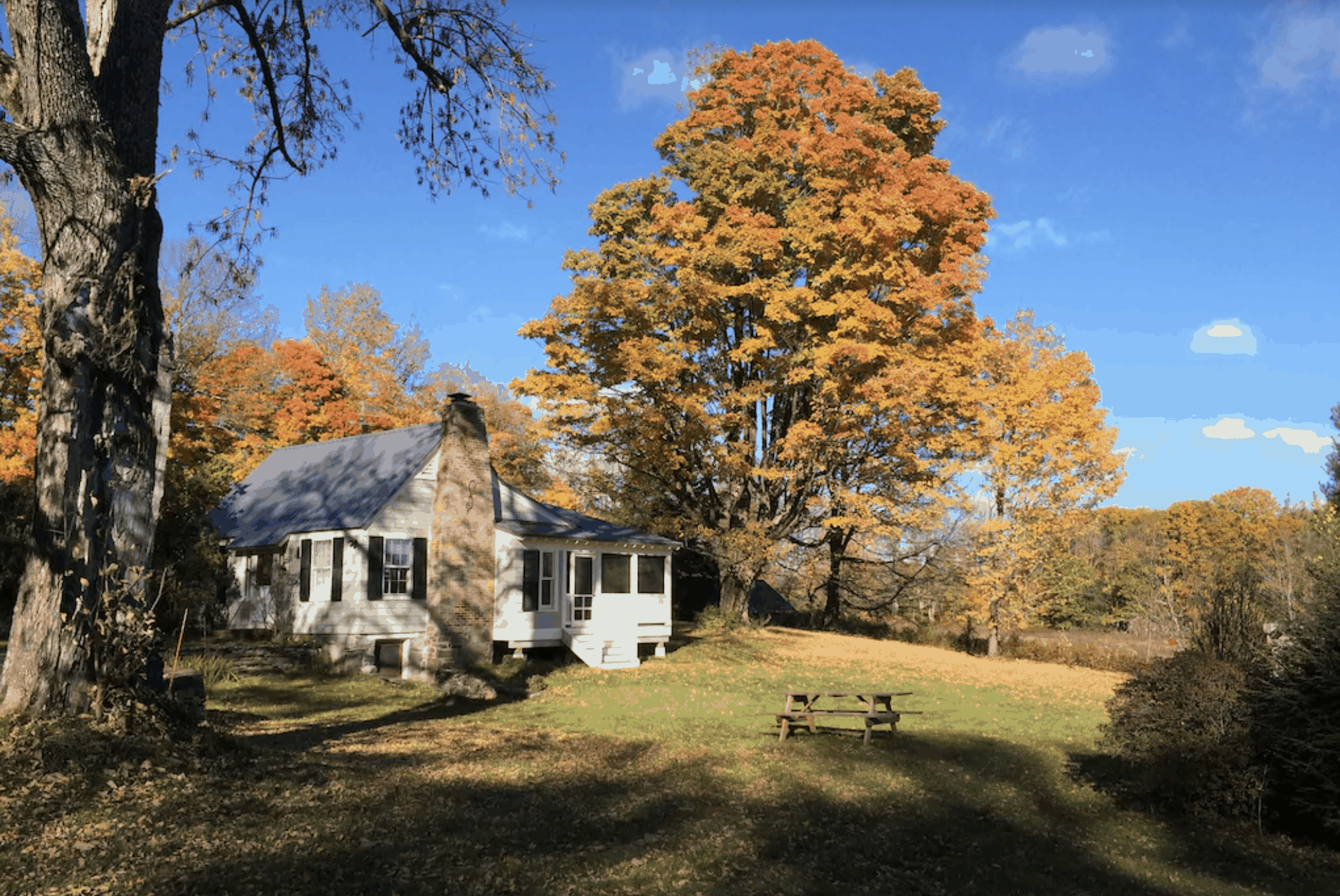 White Massachusetts vacation home with a large lawn and fall leaves on the closest trees.