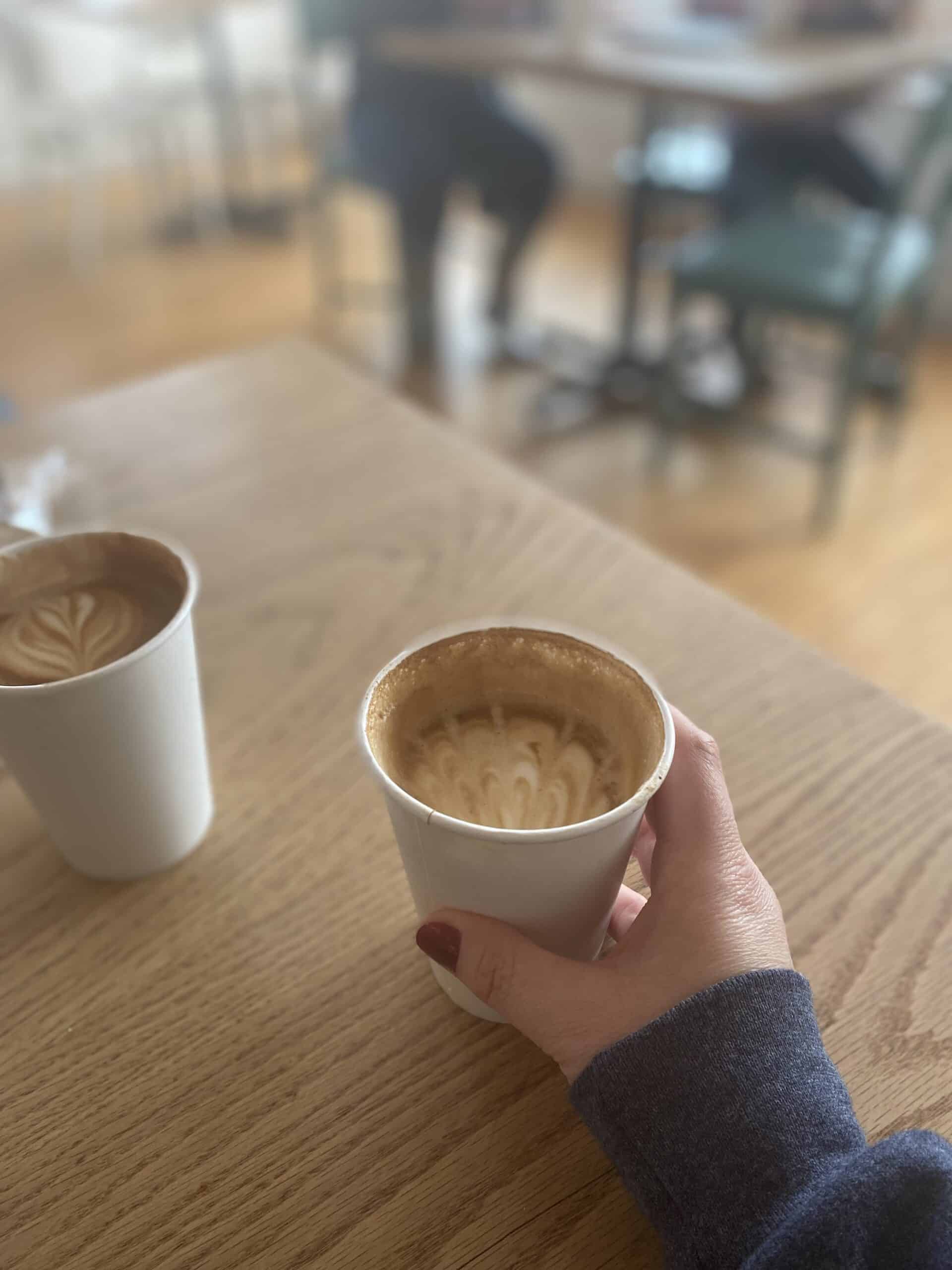 A hand holding a maple latte at a coffee shop in Stockbridge, Massachusetts