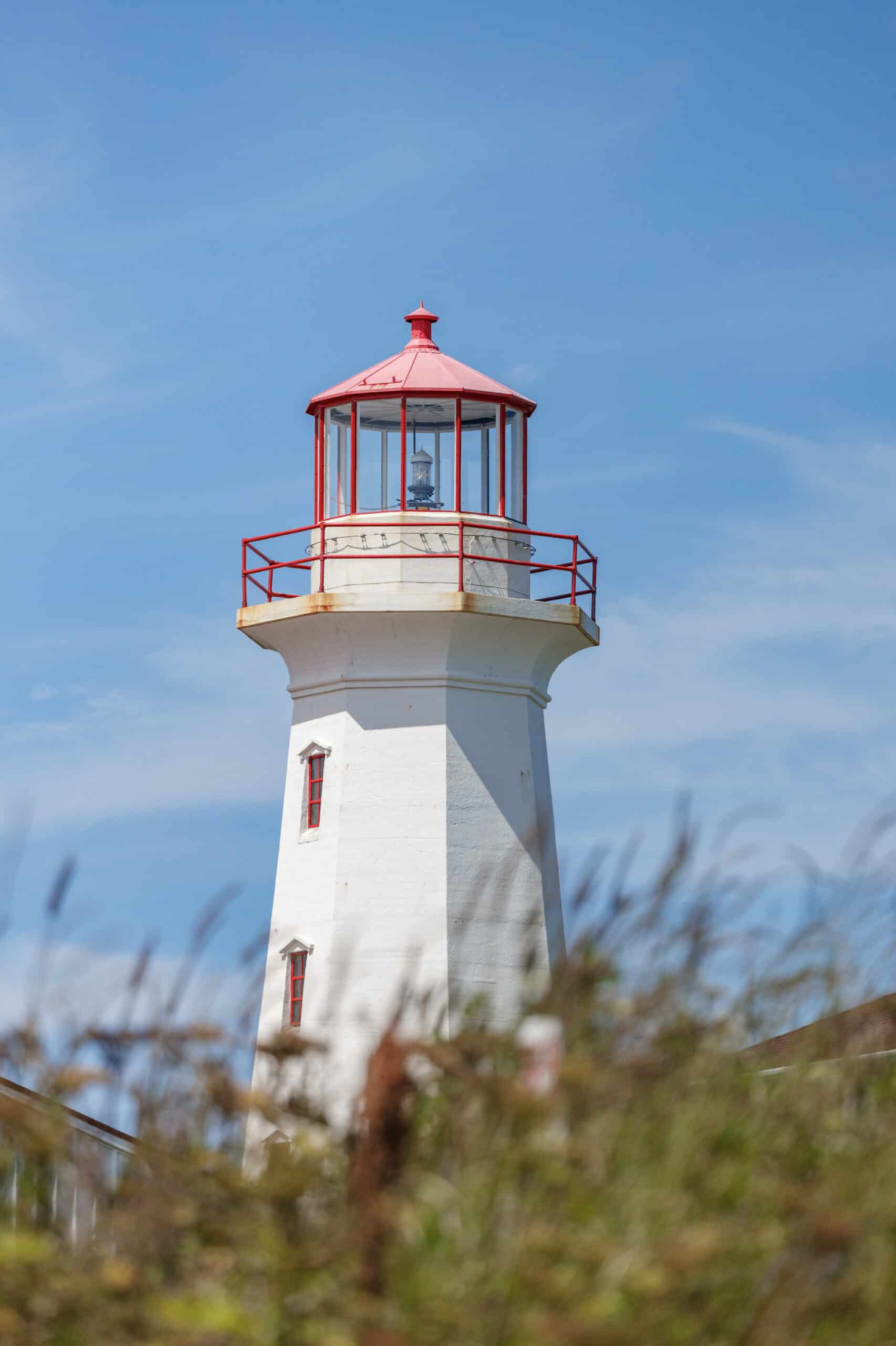 White lighthouse with red roof, railings, and window panes in Maine with blue skies in the background