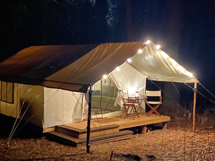 White glamping tent at night with lights on.