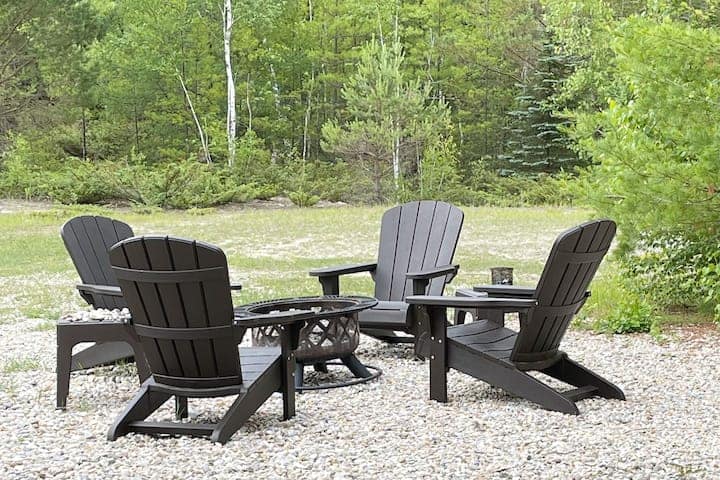 Four chairs surrounding a firepit in the woods.