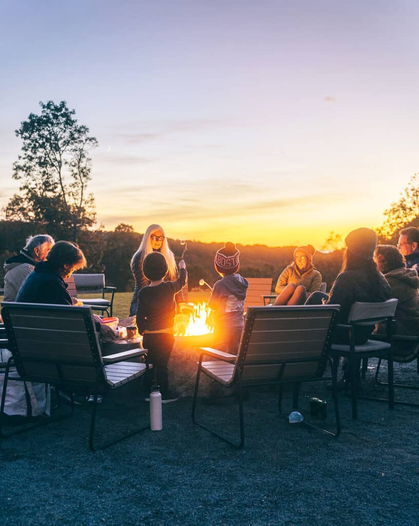 adults and kids sitting around a fire pit at sunset