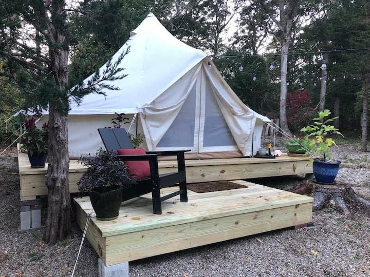 White glamping tent with a deck in the woods.