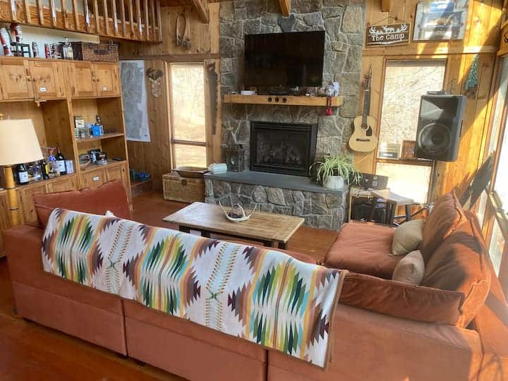 Interior of a living room with a couch, tv, and stone fireplace.