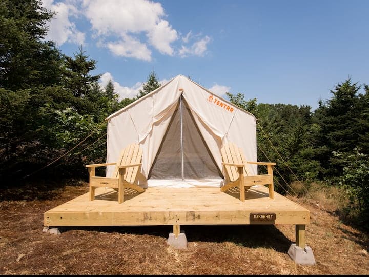 White tent with a deck in the woods under a blue sky