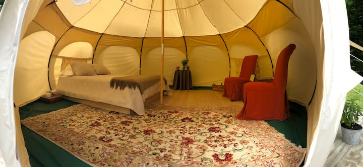 View of the inside of a yurt with a bed and red chairs.