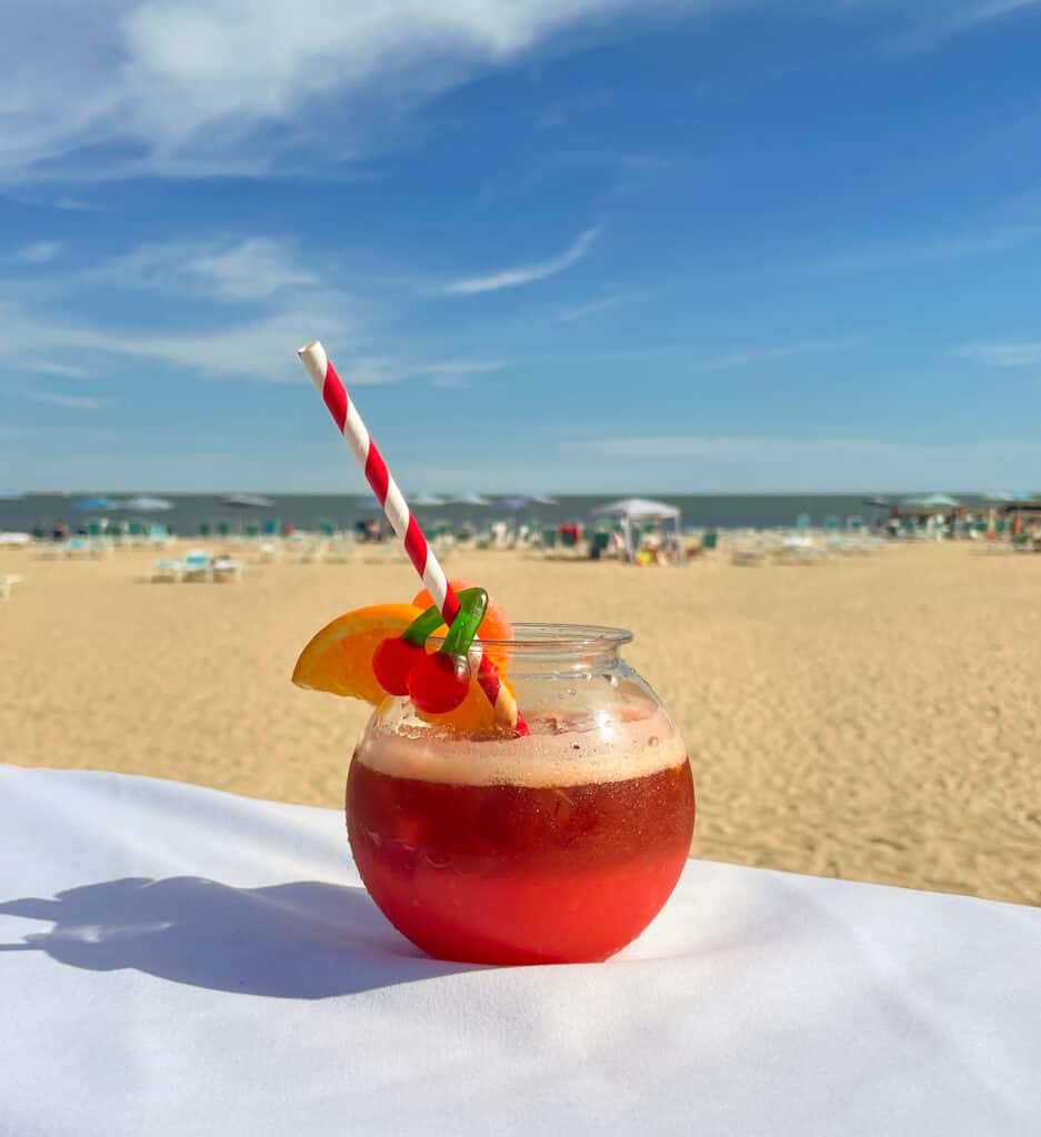 A fruity cocktail with a red and white straw on a beach in Cape Cod