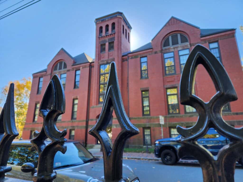 an imposing iron fence in the foreground fringes an old, stately red brick building behind