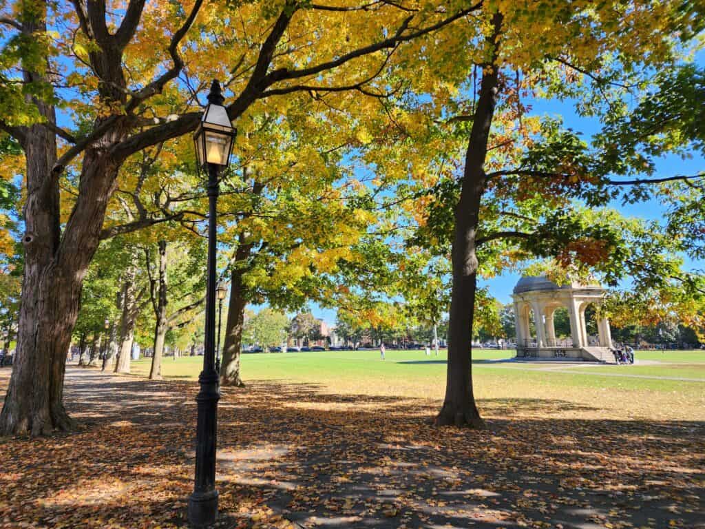 a beautiful sunny fall day in a park - the Salem Common in Salem MA, pictured are a distant white gazebo and a nearby victorian style streetlamp