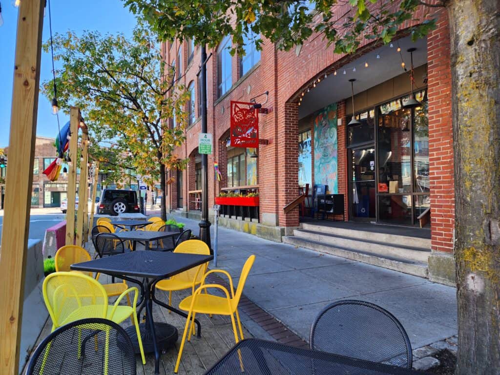 exterior of a cheerful restaurant in salem massachusetts. bright yellow chairs sit next to tables on the patio and the restaurant window is behind