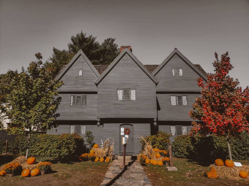 a grey and spooky image of an early american house in salem massachusetts. pumpkins and foliage surround