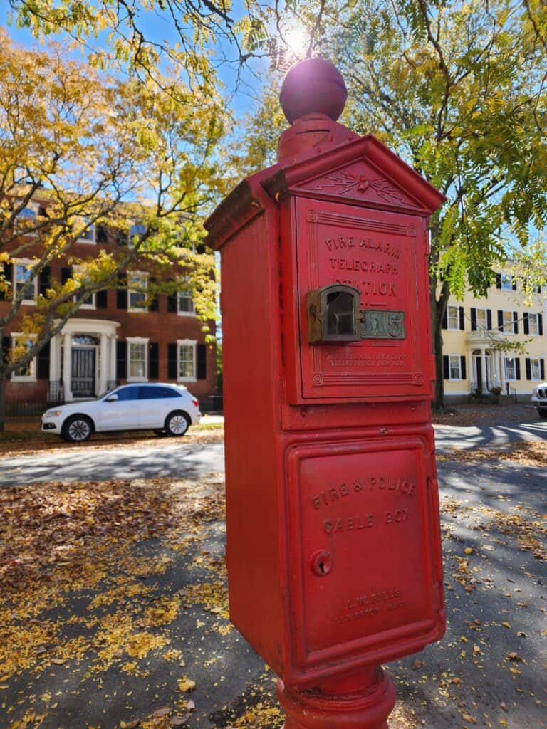 image of bright red old fashioned post box with autumn leaves and new england houses beyond