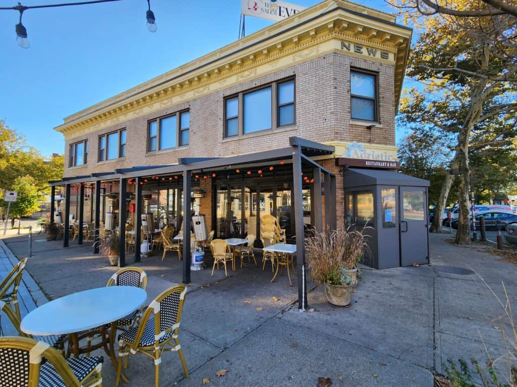 A historic building that houses one of the most popular Salem restaurants is seen with outdoor seating and string lights with a clear blue sky overhead