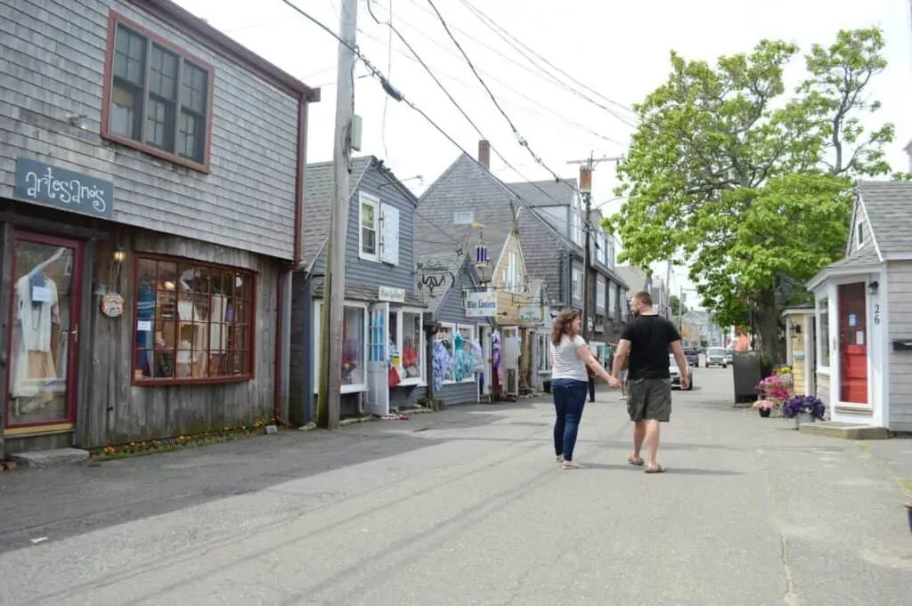 A man and woman holding hands walk down a picturesque New England street in Rockport, Massachusetts