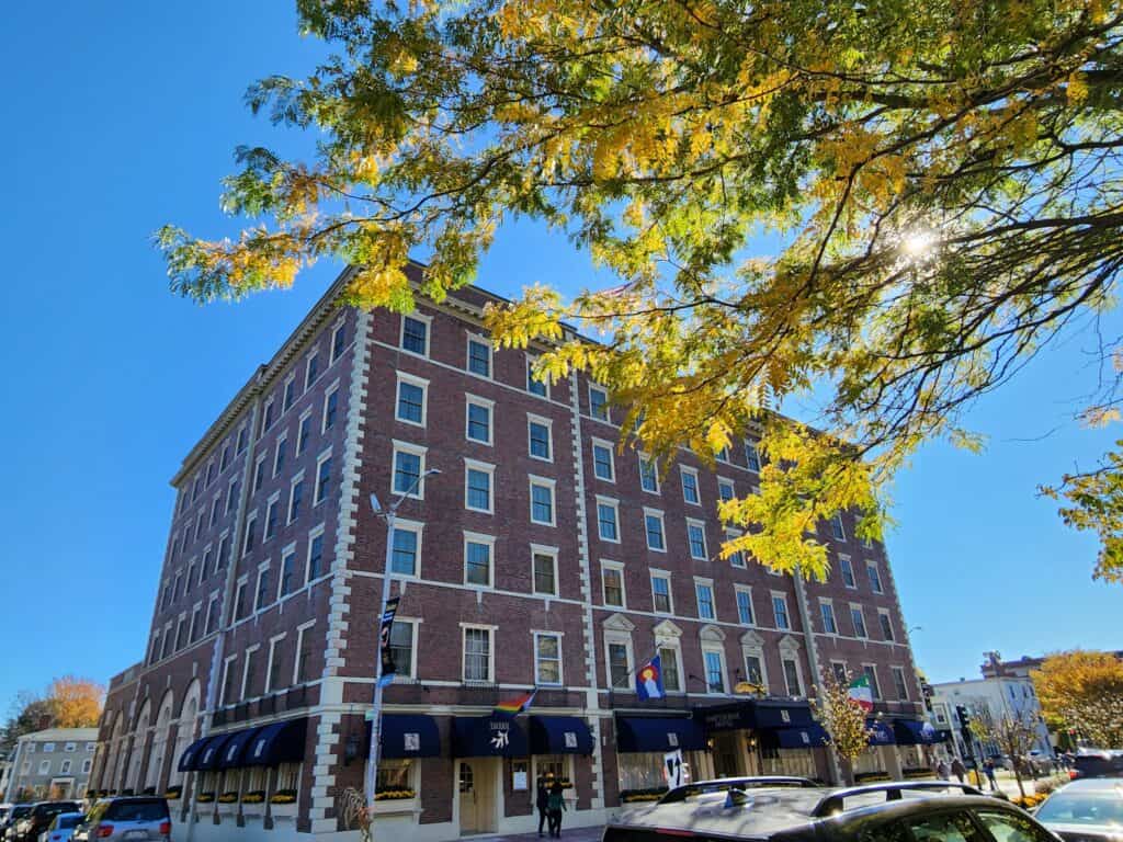 A tall red brick historic building is seen on a sunny day with autumn leaves framing the shot