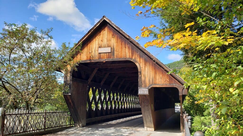 A wooden covered bridge in Woodstock, Vermont with trellis sides and foliage around it