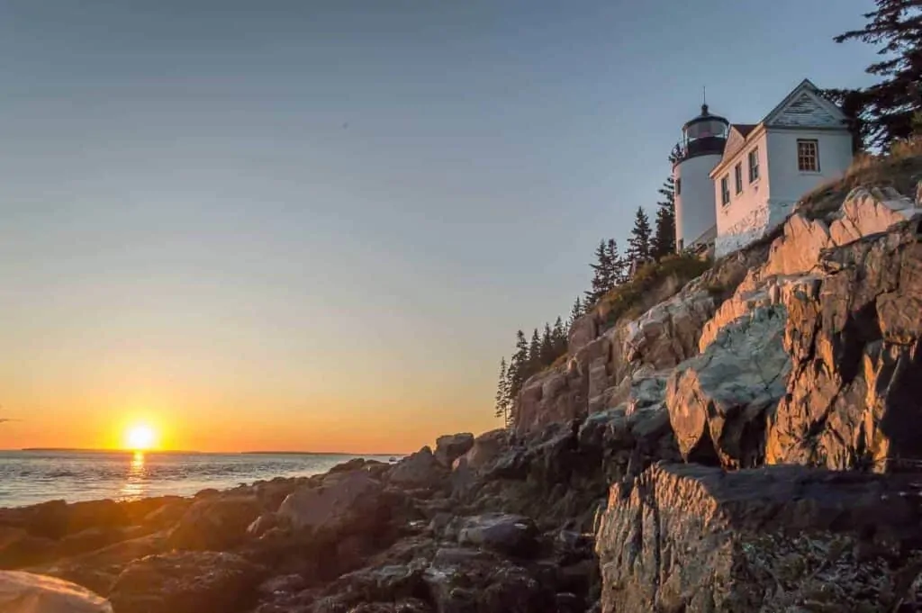 A photo of an iconic Maine lighthouse perched on a rocky cliff at sunset