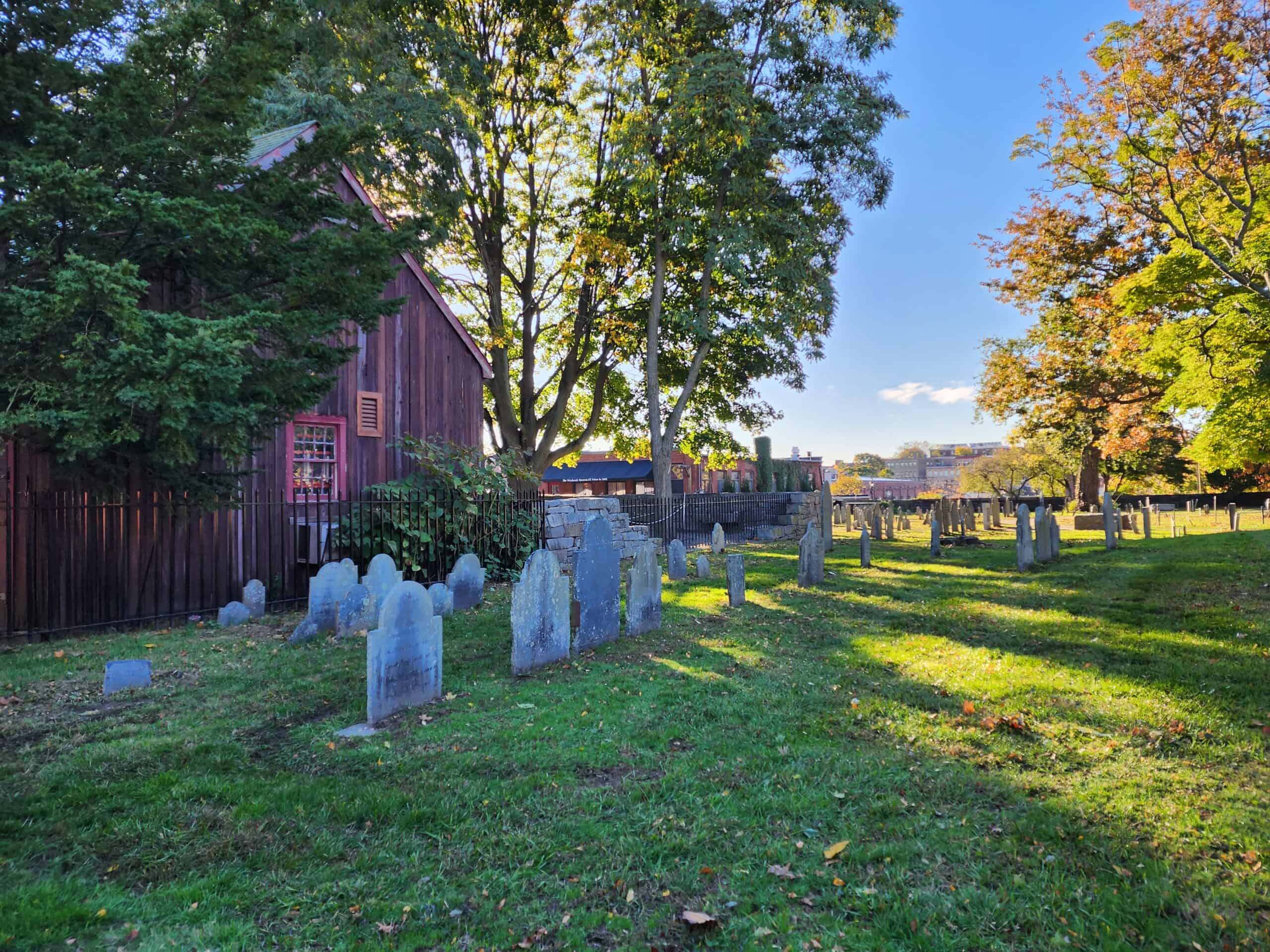 a graveyard on a sunny day; the gravestones are very very old and thin in design