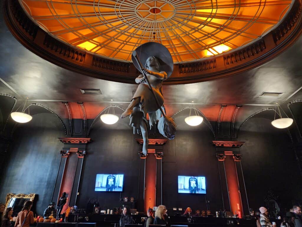interior of a shop with all black walls. a grey witch statue hangs suspended from the ceiling, orange lights above