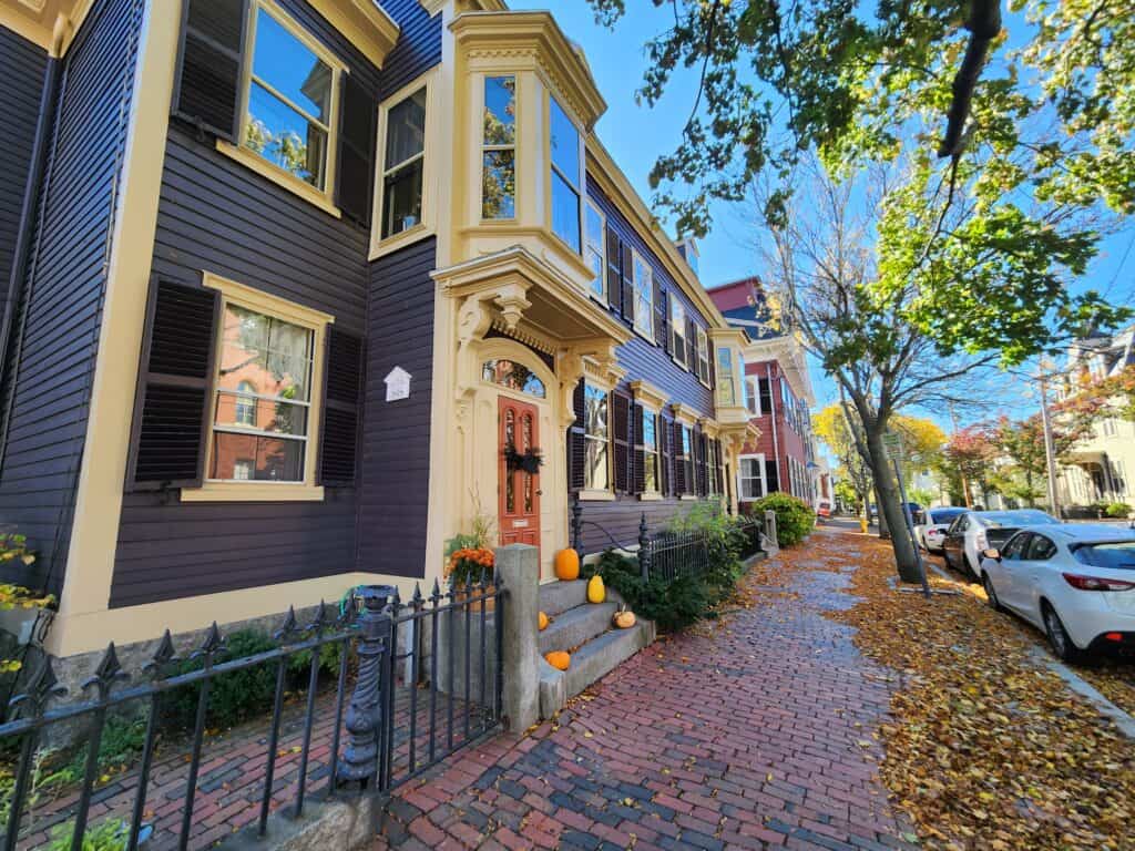 a brick lined historic street in salem with gorgeous homes. a brown home in front has pumpkins lining its steps