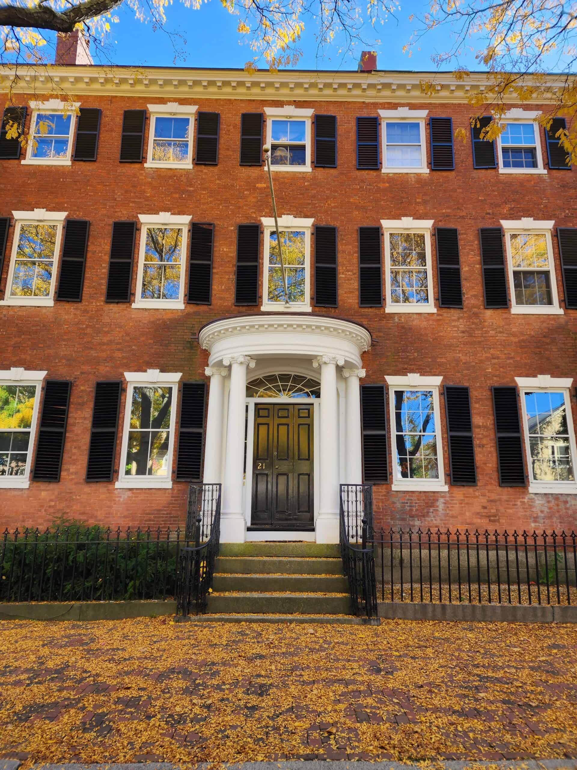 front of an elegant brick colonial home with fallen leaves covering the walkway in front