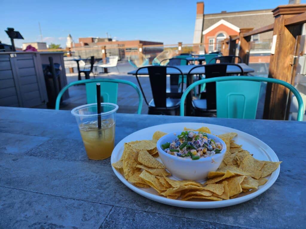 a plate of tortilla chips and dip next to a half empty cocktail in a clear plastic cup. on a table