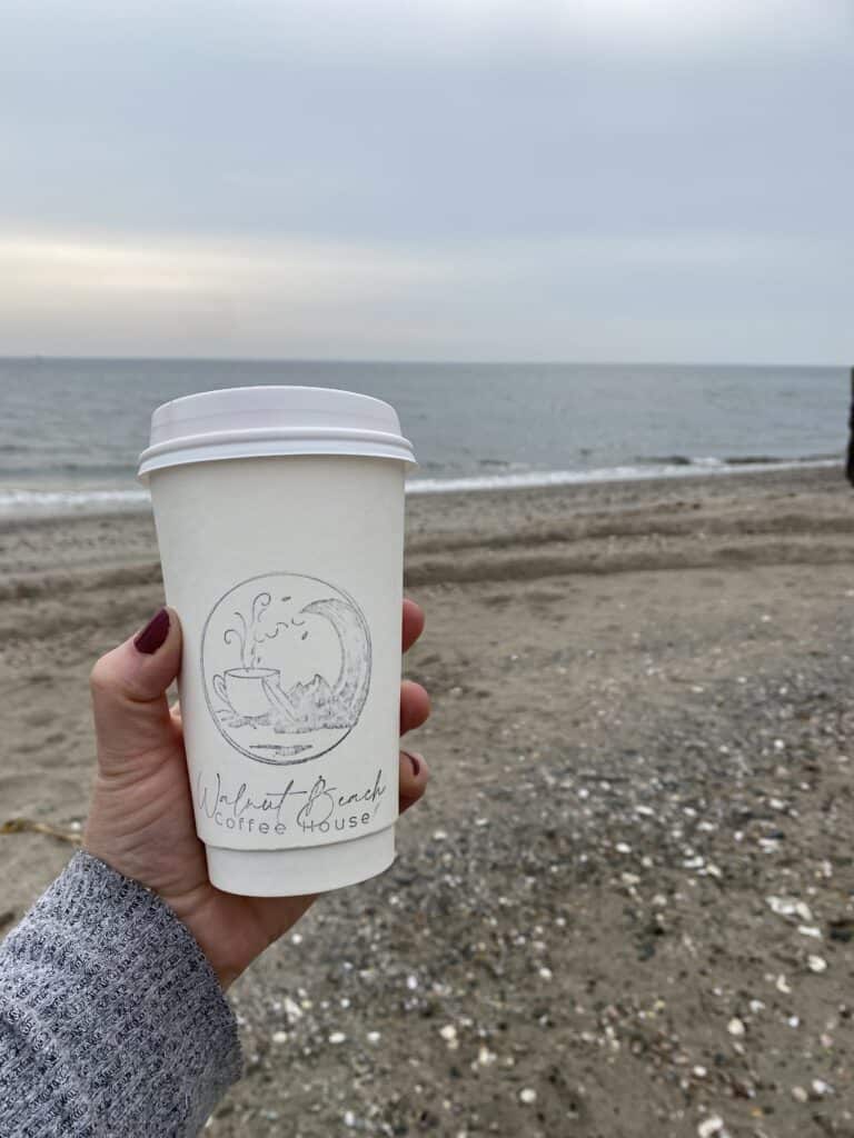 Coffee cup from Walnut Beach Coffee House in a hand in front of Walnut Beach, Connecticut