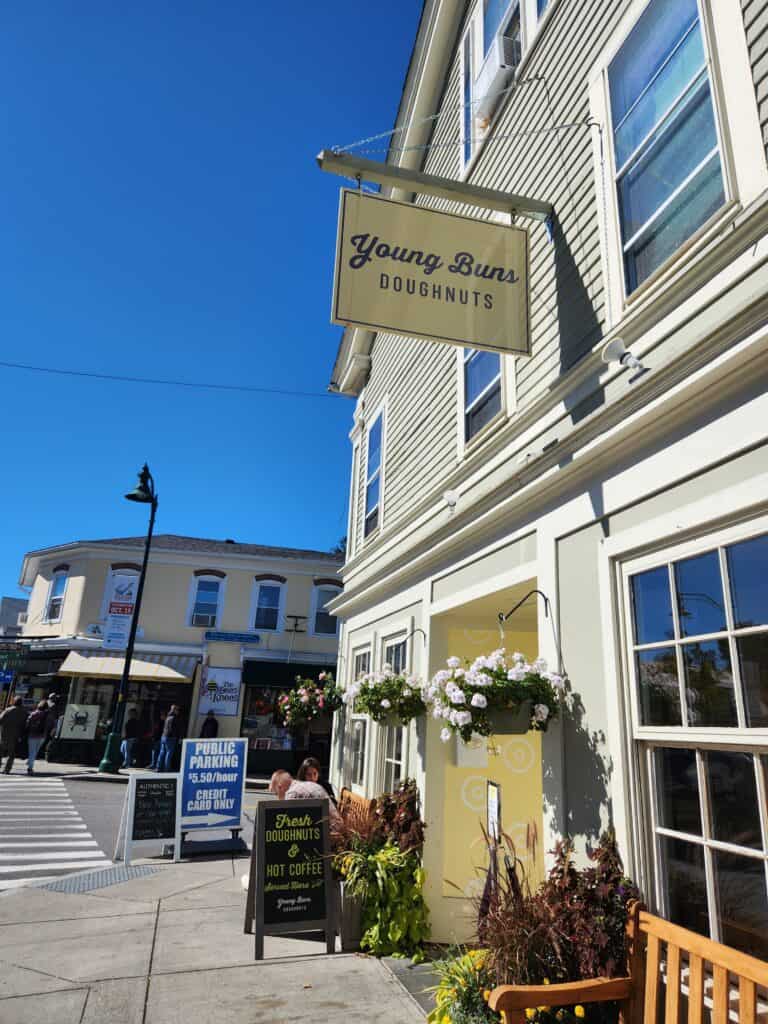 A neatly landscaped storefront for a cute Connecticut donut shop with a classic shingle style sign for donuts