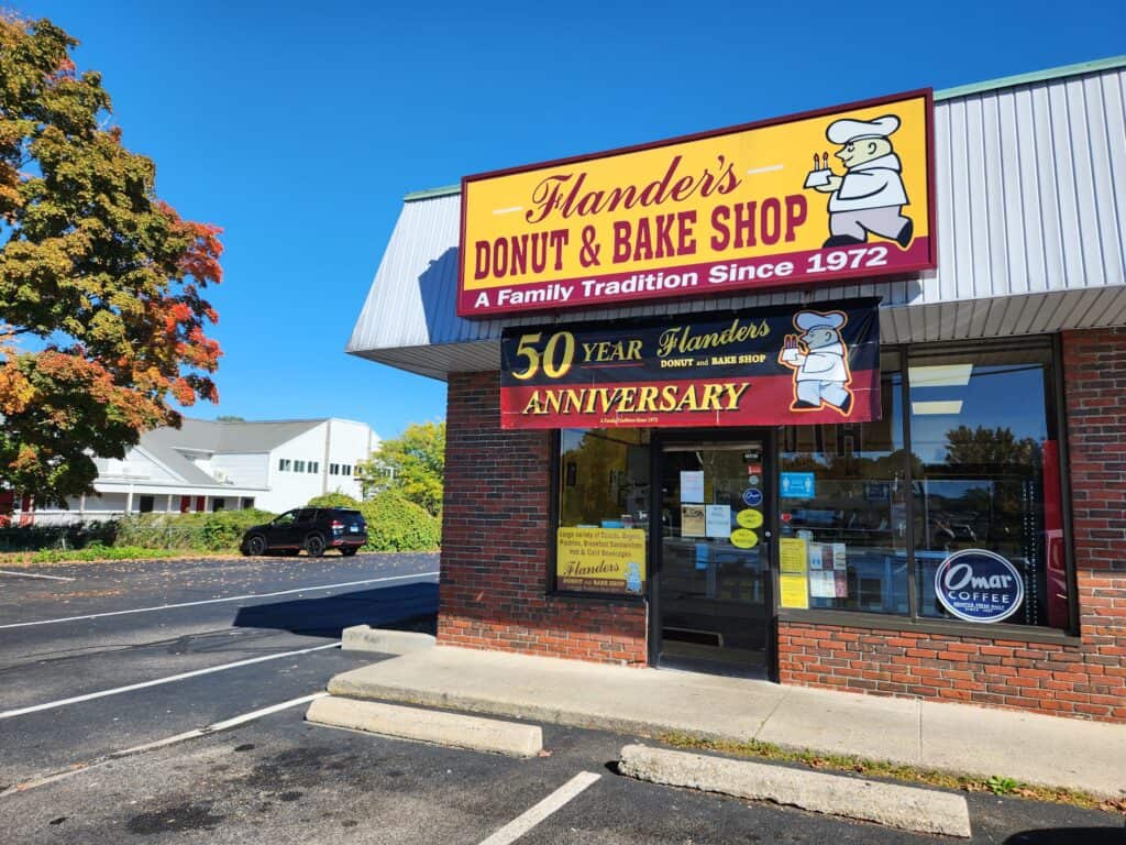 An understated sign on a CT donut shop in a traditional brick building with a small parking lot