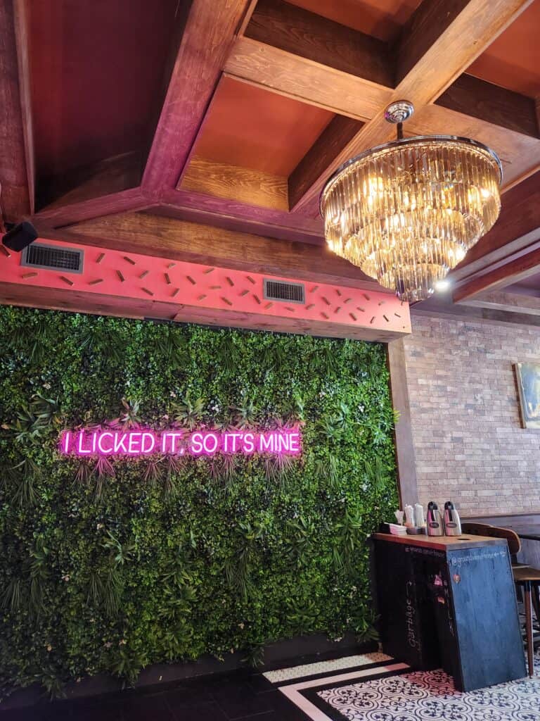 A cheeky sign that says "I licked it, so it's mine" in neonon the wall at a Connecticut doughnut shop beside an elaborate chandelier