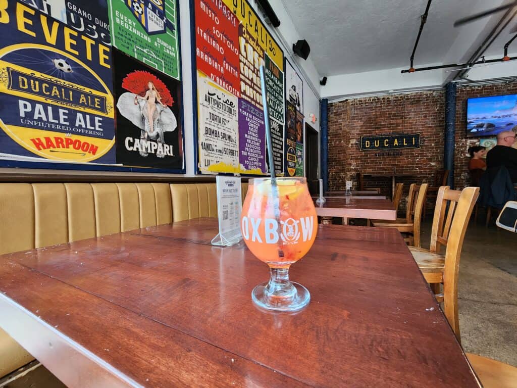 A pink beverage in a glass sits on a wooden table in a Boston North End restaurant