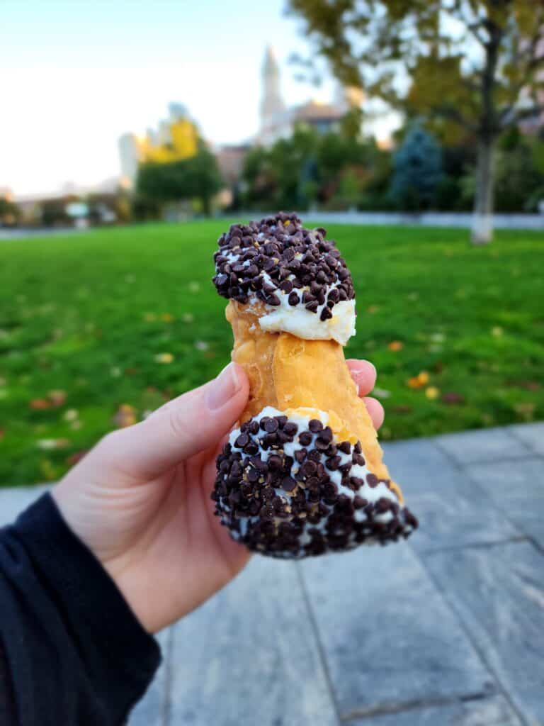 A cream filled pastry with chocolate chips at either end is held in a hand near Boston's North End neighborhood