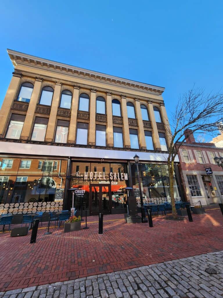 exterior image of Hotel Salem in Salem Massachusetts. a stately older building with a modern, glass-front stands on an enmpty brick-paved street