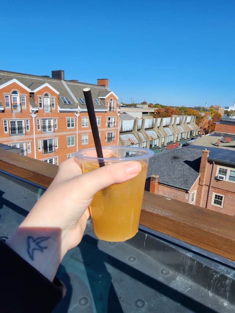 A hand holds out a drink while looking out over buildings on a rooftop in Salem MA