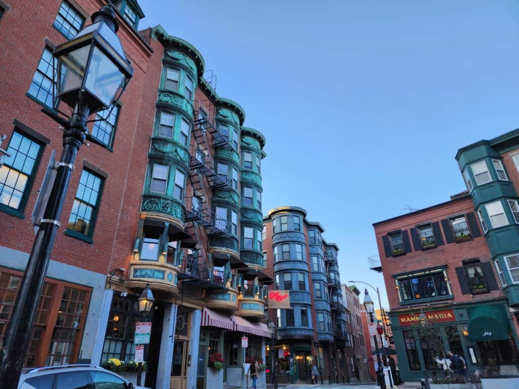 exterior of attractive buildings in boston's north end. restaurant lights are at the bottom while the top are copper windows that have gone green with age