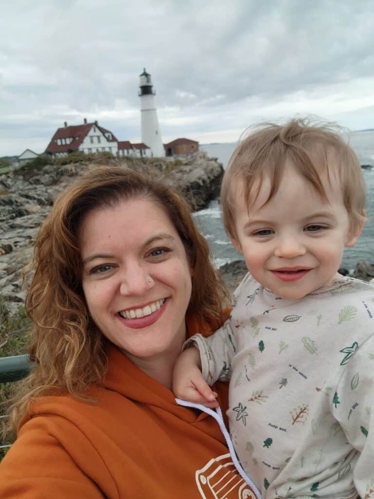 A woman and toddler pose in front of the Portland Head Light in Portland, Maine