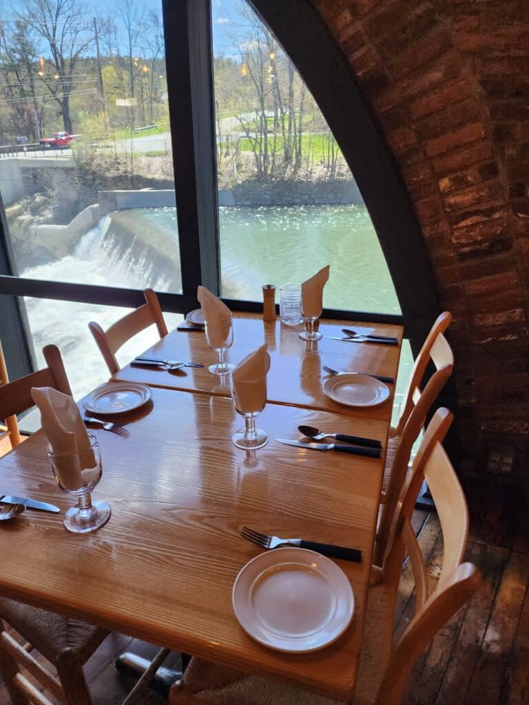 a wooden table with several place settings set against a window. outside the window is a man-made waterfall