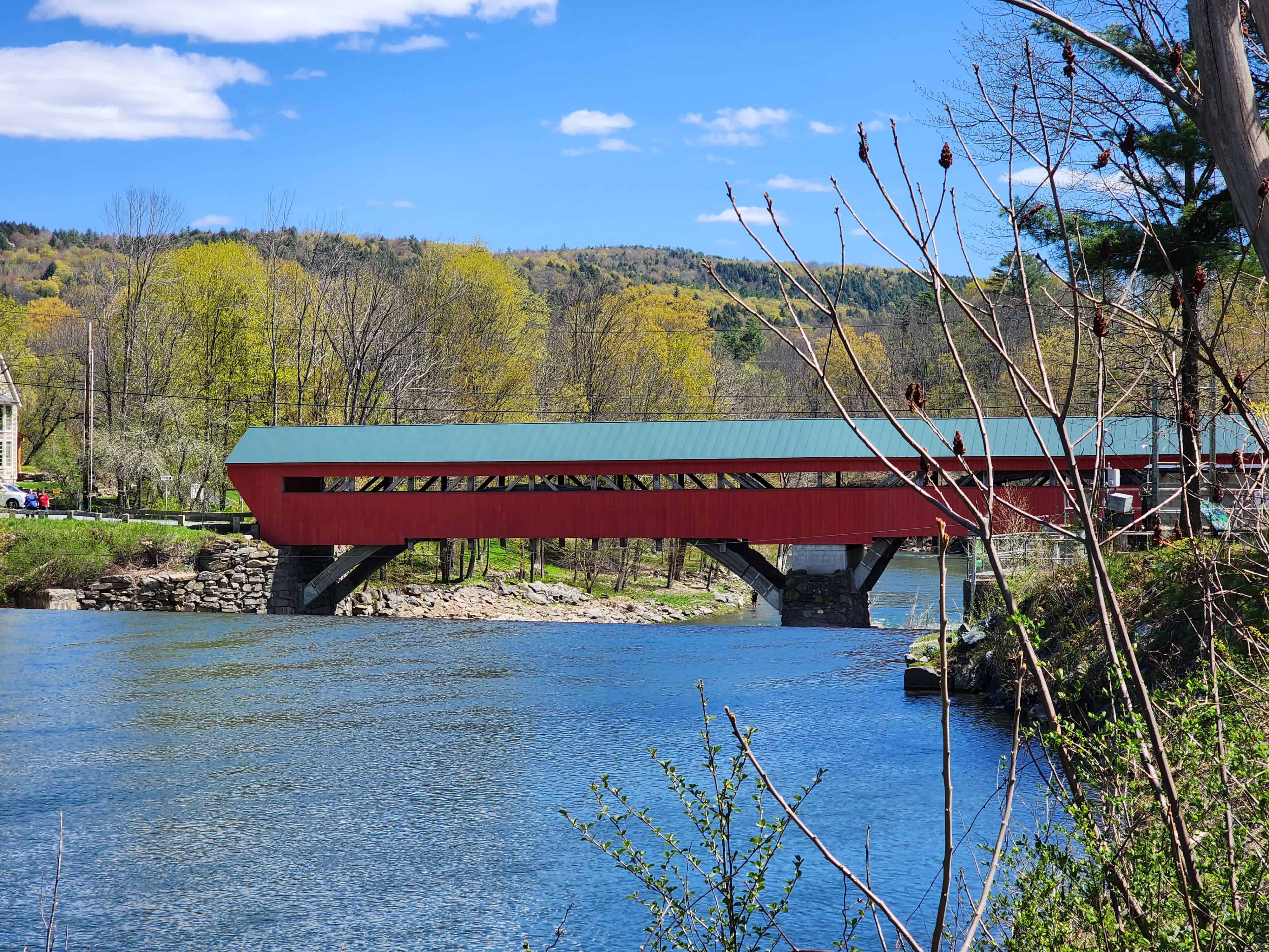 a long red covered bridge spans a calm river on a sunny day in vermont