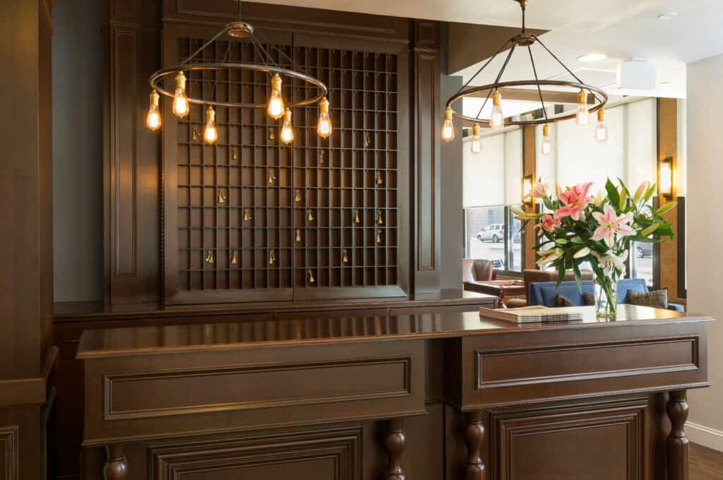 A wooden front desk with lamps overhead and a retro key hanging area behind