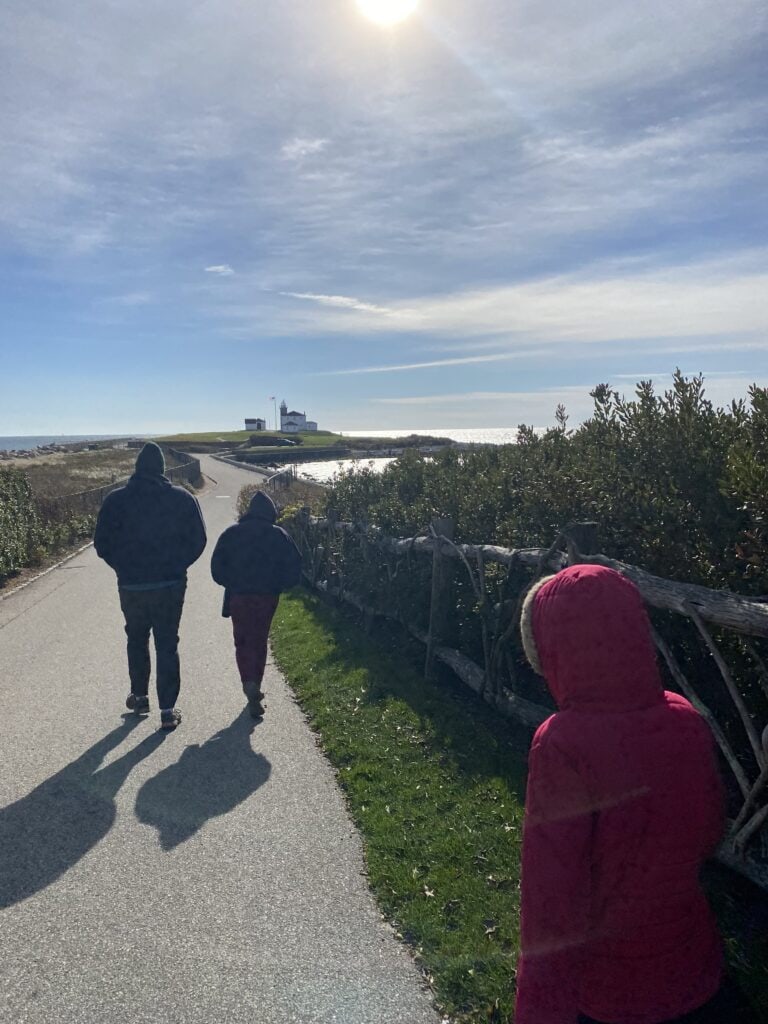 A scenic stretch of path with three people walking on it towards a popular Rhode Island lighthouse